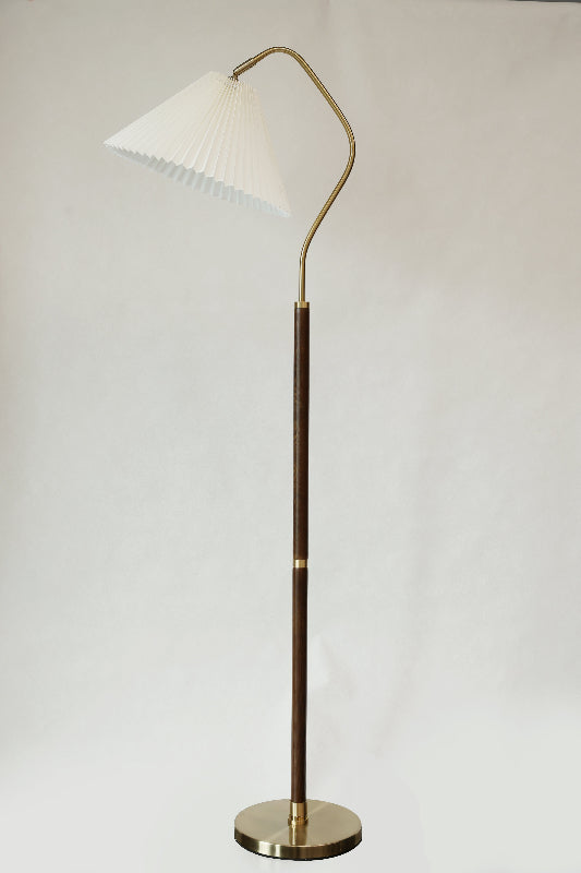 Pleated fabric shade floor lamp with a white shade and brass finish on a plain background