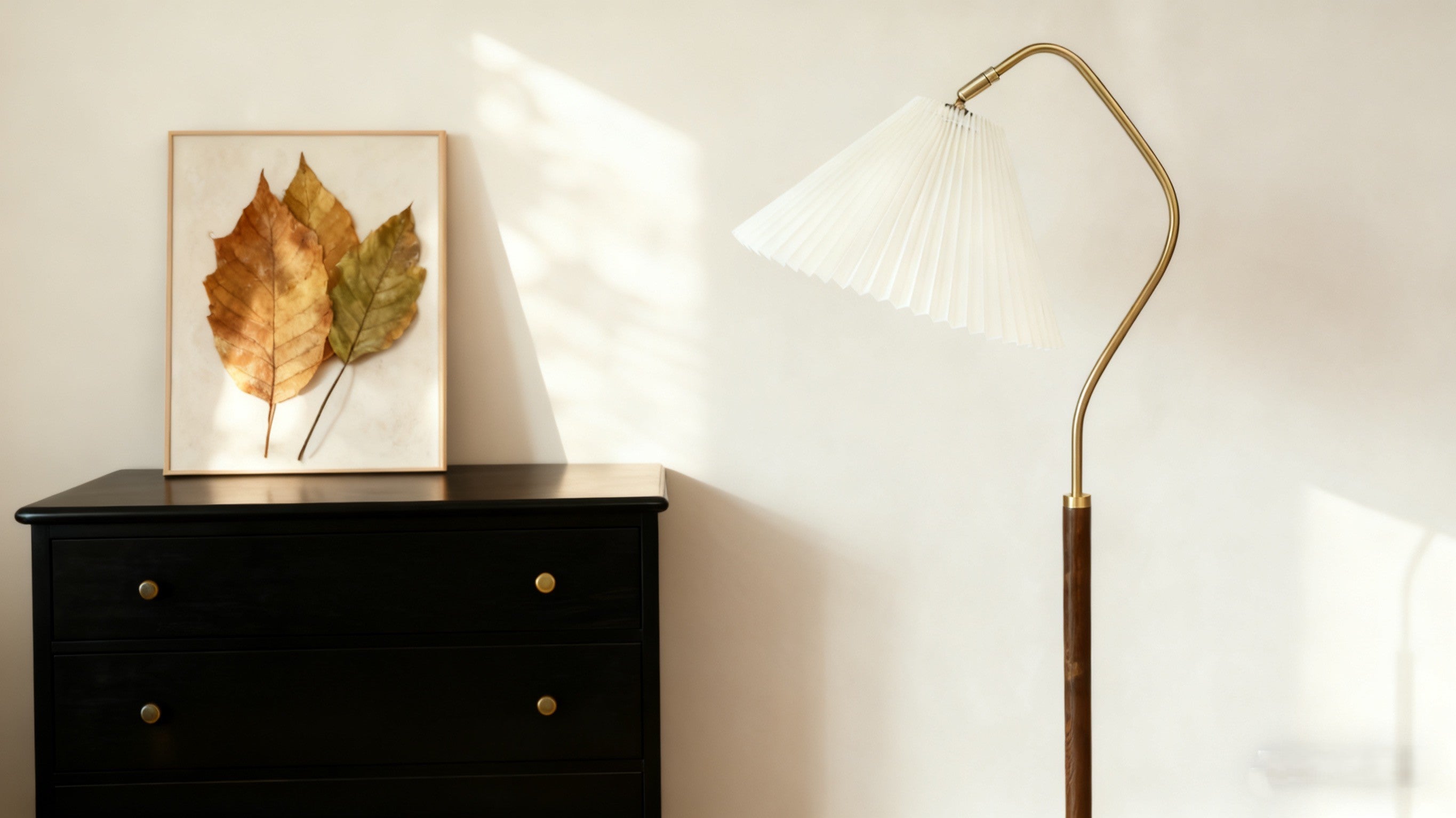 Black dresser with a gold leaf print next to a tall Homira floor lamp against a white wall.