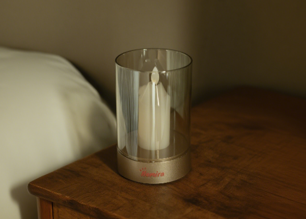 Glass candle holder with a white candle on a wooden surface in a dimly lit room.