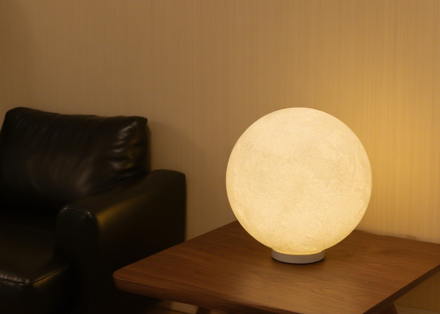 Homira moon lamp on a wooden table with a dark sofa in the background