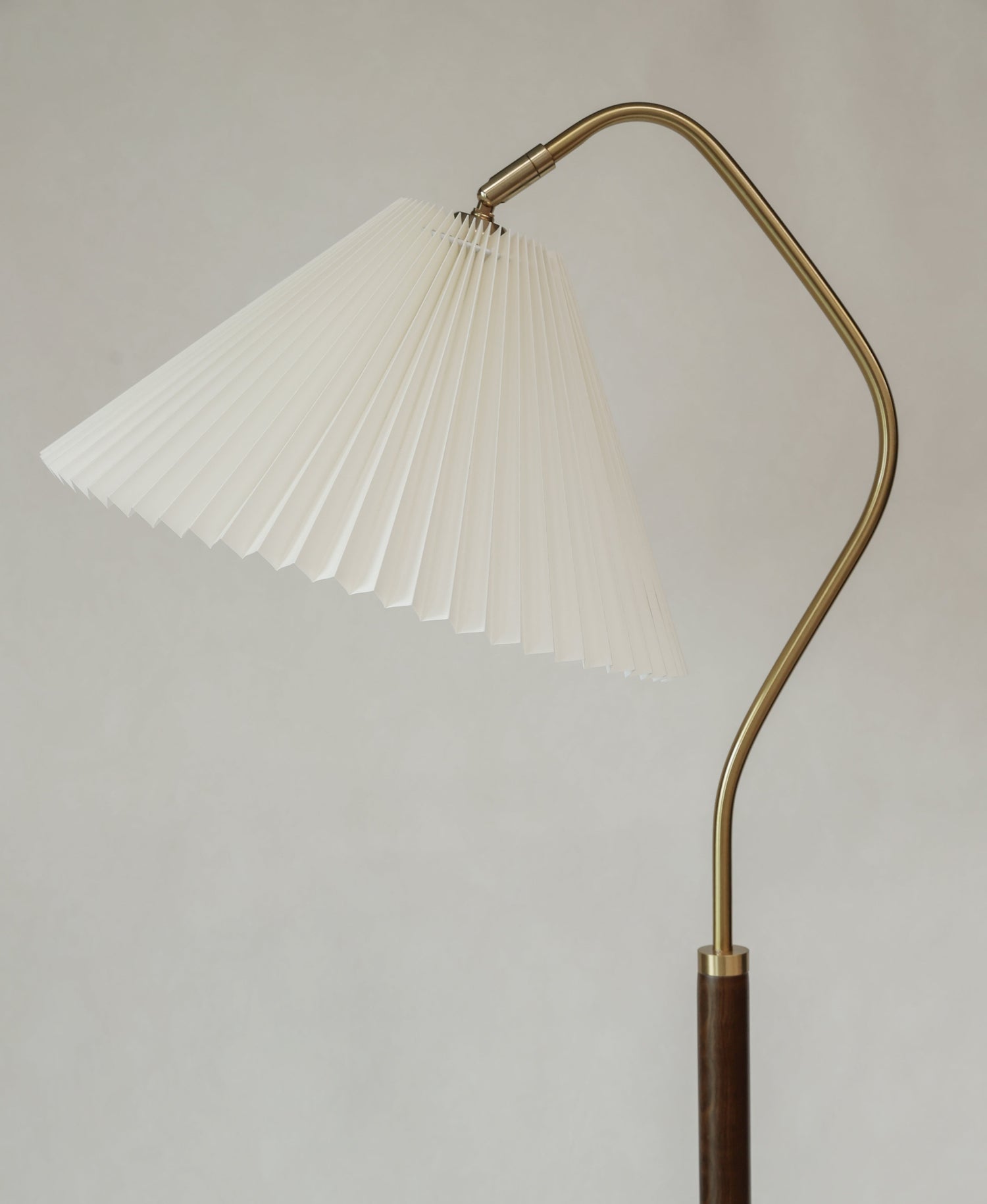 Floor lamp with pleated white shade and curved brass arm on a plain background