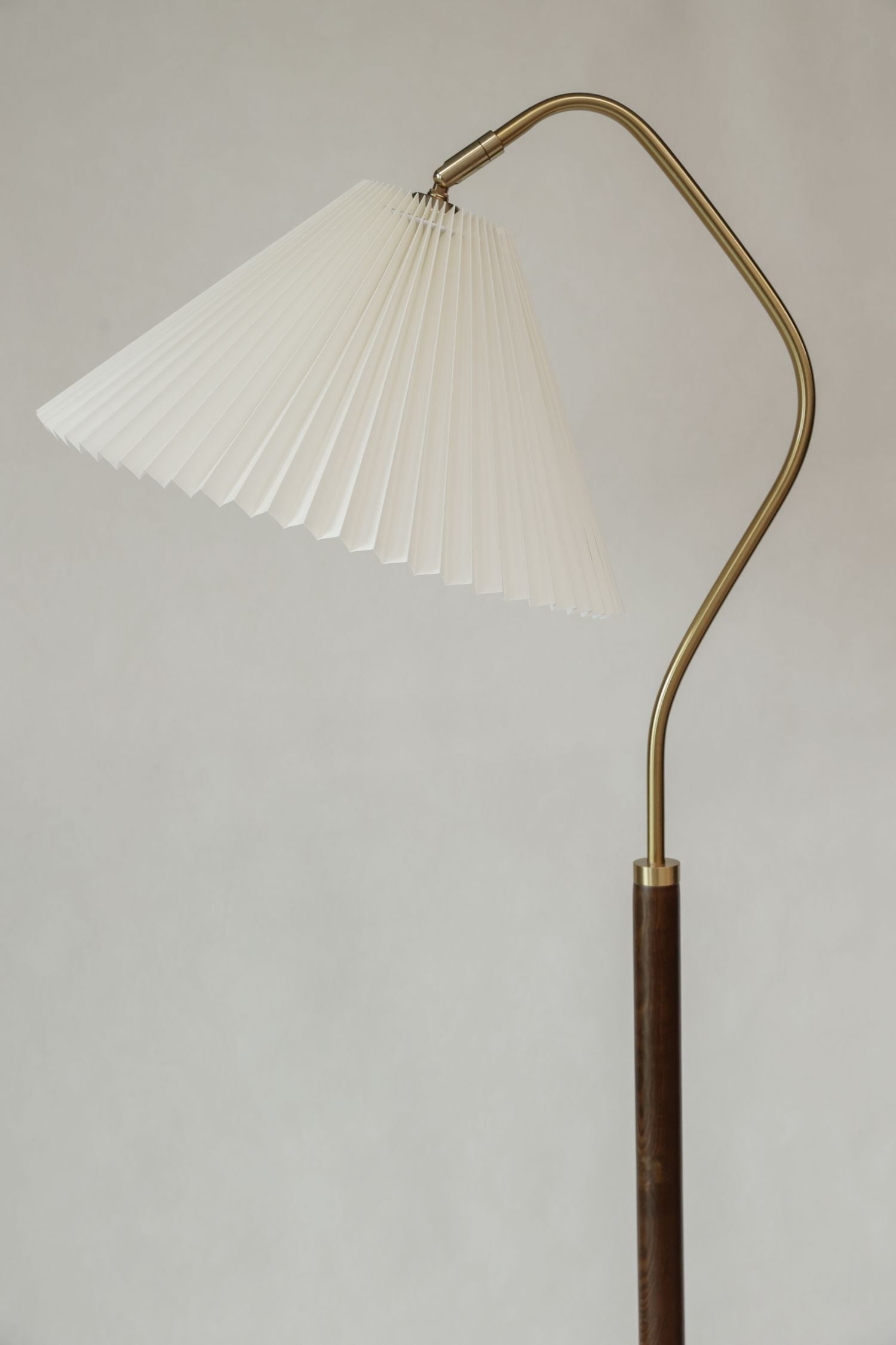 Floor lamp with pleated white shade and curved brass arm on a plain background