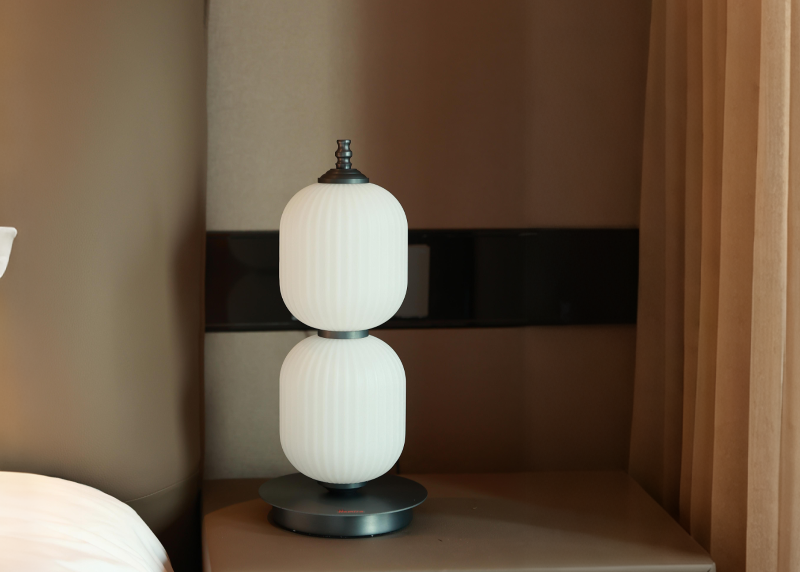 White lamp on a nightstand next to a bed with curtains in the background